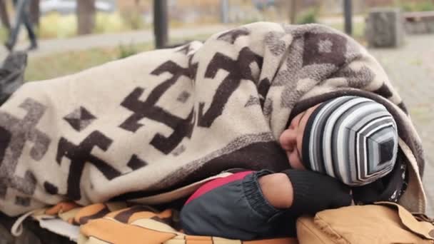 Изгой спит на скамейке в парке, одинокий бездомный мужчина пытается выжить — стоковое видео