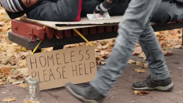 Благотворительность, добрый человек, оставляющий пачку денег на скамейке, пока бездомный мужчина спит — стоковое видео