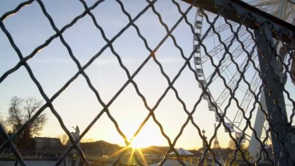 Point de vue de la personne regardant le parc d'attractions à travers une clôture de filet, coucher de soleil sur l'horizon — Video
