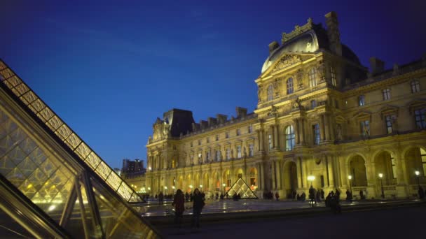 Viajeros posando cerca del gran Palacio del Louvre iluminado por la noche, visita a París — Vídeo de stock