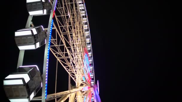 Vista lateral de la enorme rueda de la fortuna girando en el parque de atracciones bajo el cielo oscuro de la noche — Vídeos de Stock