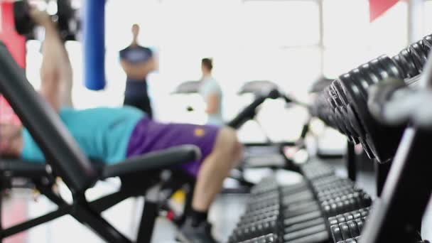 Silueta desenfocada del joven haciendo ejercicio de prensa de banca de mancuerna en el gimnasio — Vídeos de Stock