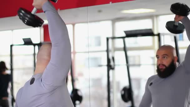 Male heavyweight athlete exercising with dumbbell in front of mirror in gym — Stock Video