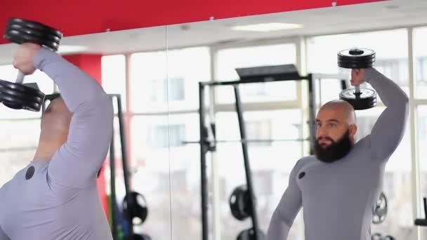 Atleta masculino haciendo ejercicio con pesadas mancuernas en el gimnasio, mirando el reflejo del espejo — Vídeo de stock