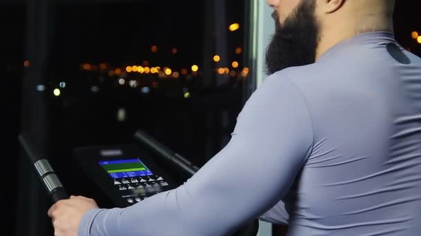 Бородатый мужчина смотрит на ночной городской пейзаж через окно после тренировки в тренажерном зале — стоковое видео