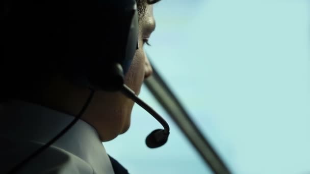 Serious male pilot focused on flight navigation, talking to air controller — Stock Video