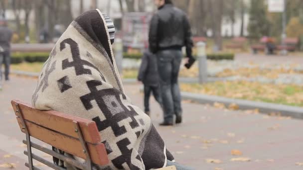 Психически больной человек прячется под одеялом, счастливые люди гуляют в осеннем парке — стоковое видео