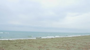 Fırtınalı deniz, gri bulutlar ufukta. Plajda çalışan genç esmer kadın