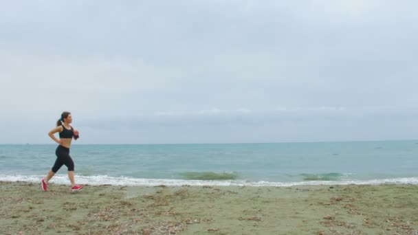 Όμορφο κορίτσι τζόκινγκ κατά μήκος της θάλασσας. Αλμυρή κύματα εκτίναξη προς άδειο αμμώδη παραλία — Αρχείο Βίντεο