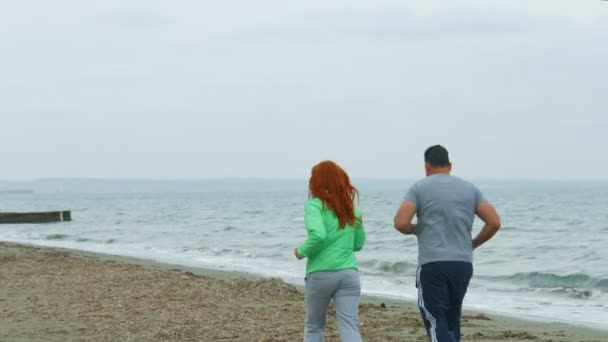 Пара средних лет бегает по морскому пляжу утром. Здоровый образ жизни — стоковое видео