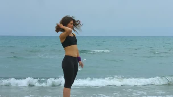 Ung kvinna tittar på salta vågor stänker på stranden, dricka friskt vatten — Stockvideo