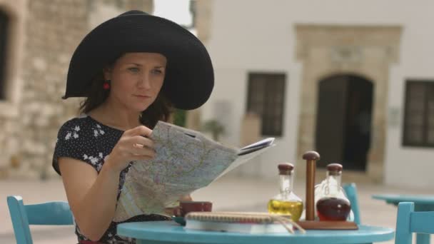 Pretty female tourist sitting in cafe with map in hands, examining journey route — Stock Video