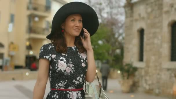 Happy young woman walking with luggage in hands, talking on smartphone, smiling — Stock Video