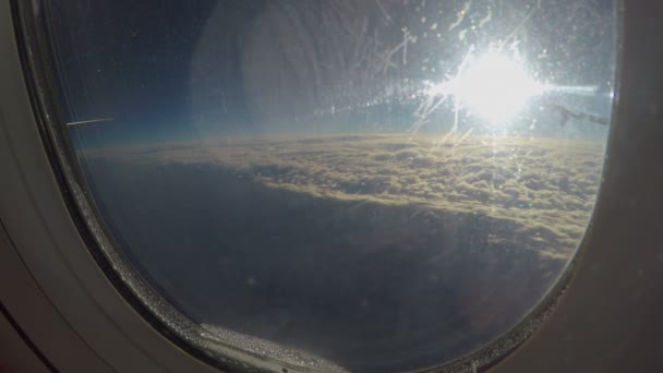 Vista do sol brilhando sobre a paisagem nublada através da janela suja do avião voando no céu — Vídeo de Stock