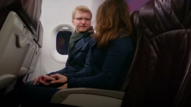 Glücklicher junger Mann und Frau, die bequem im Flugzeug sitzen, Händchen halten, reden — Stockvideo