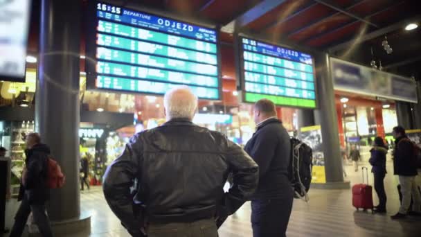 프라하, 체코 - 2015년 12월경: 기차역 승객. 열차를 기다리는 남성 승객 2명, 디스플레이 화면에서 시간표 확인 — 비디오