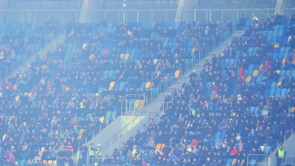 Åskådarna sitter på tribuner och tittar på fotbollsmatch, kallt väder, dimma — Stockvideo