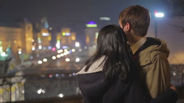 Jovem casal romântico no amor abraçando e olhando para paisagem urbana noite incrível — Vídeo de Stock
