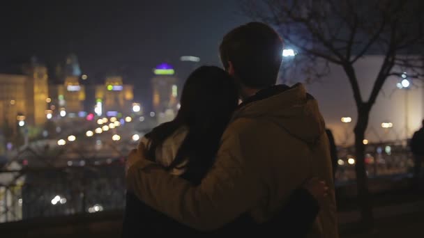 Pareja enamorada abrazándose suavemente, mirando al futuro juntos, paisaje urbano nocturno — Vídeo de stock
