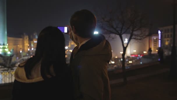 Счастливые парень и девушка делают селфи на смартфоне, свидание в ночном городе — стоковое видео