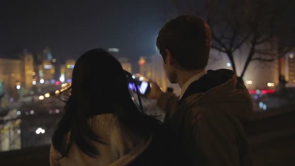 Pareja joven enamorada tomando selfie y besándose en una cita romántica, paisaje urbano nocturno — Vídeos de Stock