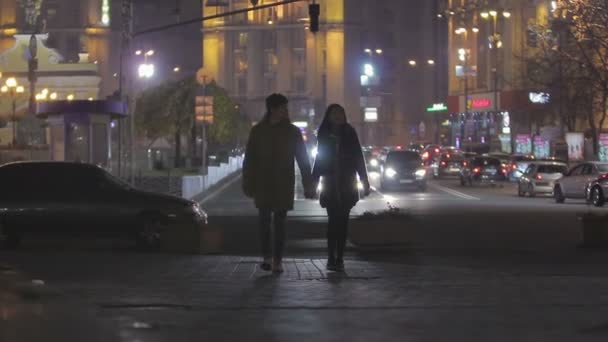 Adolescentes felices enamorados caminando por la calle de la ciudad nocturna, tomados de la mano y abrazados — Vídeo de stock