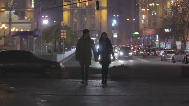 Adolescentes felices enamorados caminando por la calle de la ciudad nocturna, tomados de la mano y abrazados — Vídeos de Stock