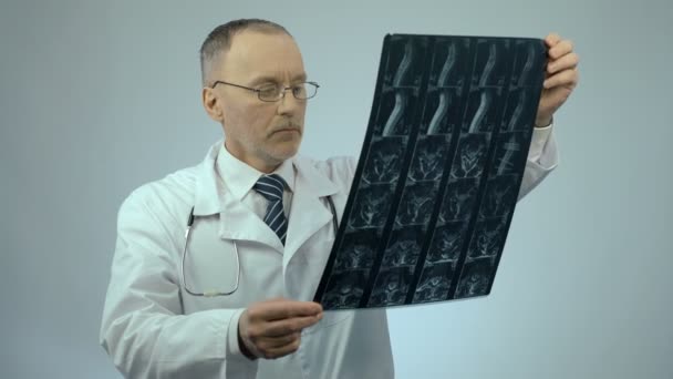 Médico serio revisando imagen de escaneo de columna lesionada, mirando a la cámara — Vídeos de Stock