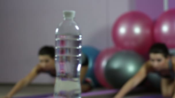 Cambio de enfoque de mujer flexible que se estira en el gimnasio a botella de agua dulce — Vídeos de Stock