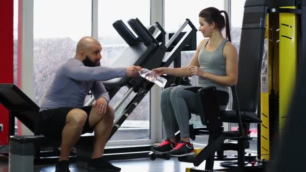 Hombre dando botella de agua potable fresca a la mujer durante el entrenamiento activo en el gimnasio — Vídeo de stock