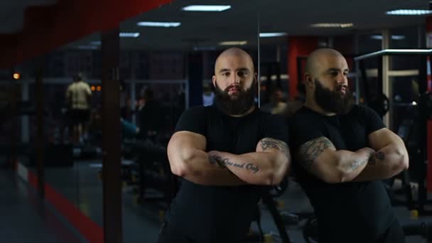 Hombre musculoso seguro de sí mismo mirando a la cámara, la gente haciendo ejercicio en el gimnasio, espejo — Vídeo de stock