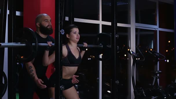 Muscular personal trainer ajudando mulher sexy para fazer exercício de barbell no ginásio — Vídeo de Stock