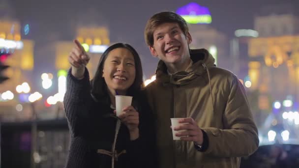 Молода щаслива пара насолоджується нічним вуличним шоу, п'є чай, розважається на відкритому повітрі — стокове відео