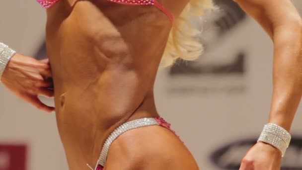 Beautiful female bodybuilder taking side and rear poses to demonstrate fit body — Stock Video