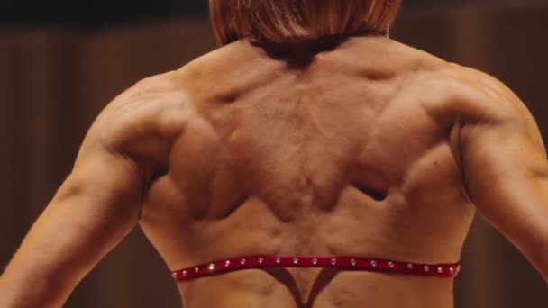 Feminino fisiculturista em pé na parte traseira lat e relaxado lado poses para mostrar músculos — Vídeo de Stock