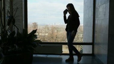 Büyük pencere duran ve konuşan uzun saçlı esmer kadın