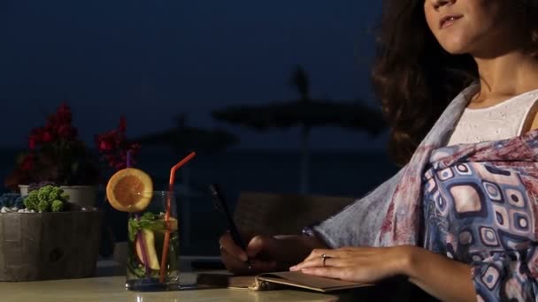 Hermosa poetisa beber refresco en la cafetería de la playa, escribir novela en cuaderno — Vídeo de stock