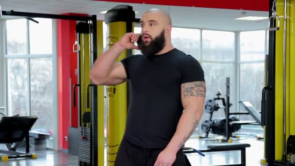 Hombre deportivo exitoso con cuerpo fuerte en forma hablando por teléfono en el gimnasio — Vídeos de Stock