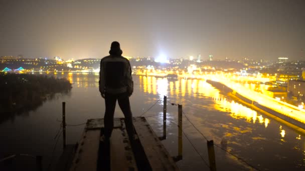 Медитация на краю моста ночью, человек наслаждается фантастическим видом на город — стоковое видео