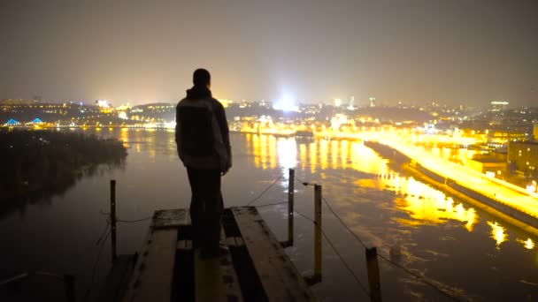 Ευχαριστημένος άνθρωπος ψάχνει τη νύχτα πόλη από την κορυφή της γέφυρας, αυξάνοντας τα χέρια του, νίκη — Αρχείο Βίντεο