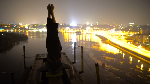 Hombre fuerte haciendo cabecera en el puente por la noche, autocontrol, equilibrio — Vídeos de Stock