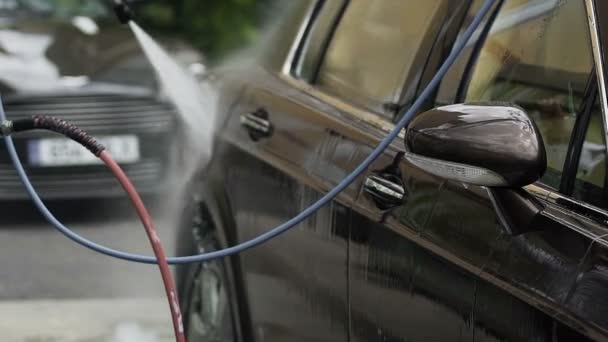 Werknemer reinigen van auto's, het sproeien van water over voertuig, succesvolle Autowassen business — Stockvideo