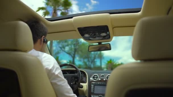 Conduite dans la ville de villégiature par une journée ensoleillée, vue sur le conducteur masculin depuis le siège arrière de la voiture — Video