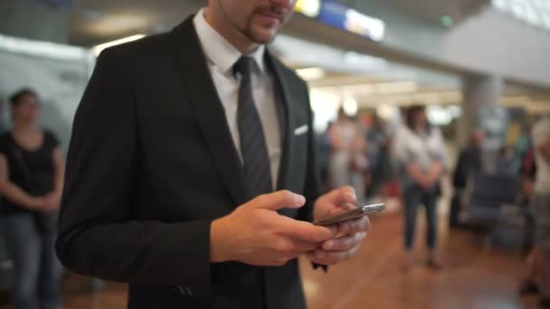 Бізнесмен стоїть в залі аеропорту, вводить повідомлення по телефону, ділова поїздка — стокове відео