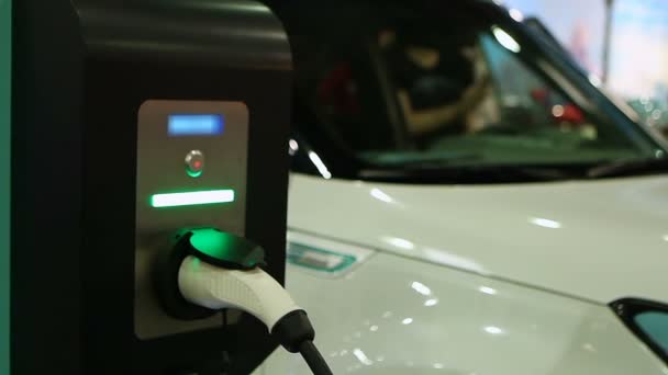 Жінка тестує електричний автомобіль на автосалоні, автомобіль підключений до точки заряджання — стокове відео