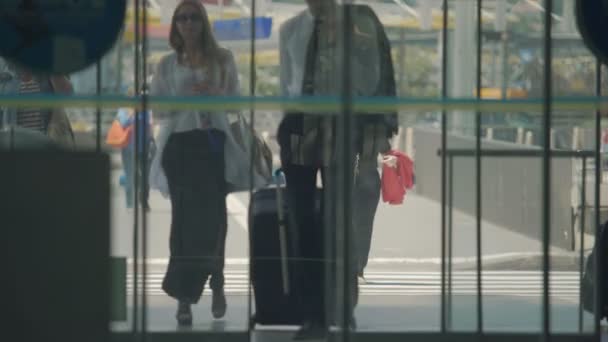 Мужчина и женщина в длинном платье входят в зал аэропорта через автоматическое открытие дверей — стоковое видео