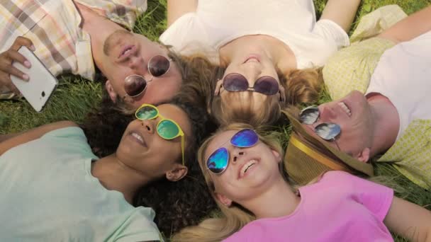 Αγόρια και κορίτσια, Παρατηρώντας αστεία βίντεο στο τηλέφωνό ξαπλωμένοι στο γρασίδι, ευτυχία — Αρχείο Βίντεο