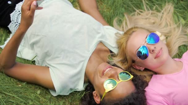 Señoras en gafas de sol disfrutando del verano, tumbado en la hierba, navegar por la web en el teléfono inteligente — Vídeos de Stock