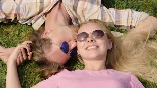 Young couple lying on grass, holding hands, boyfriend kissing girlfriend, date — Stock Video