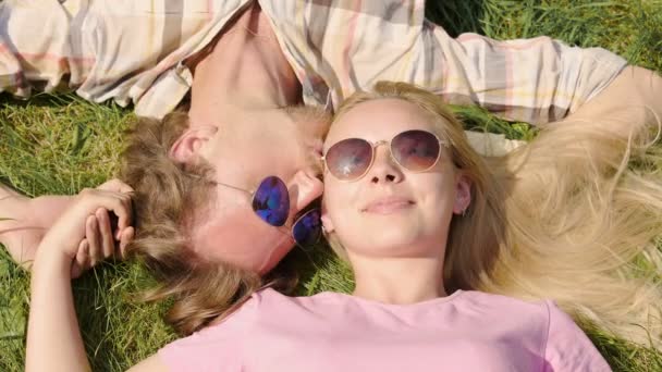 Junge glückliche Familie im Gras liegend, küssend, Händchen haltend und Urlaub genießend — Stockvideo